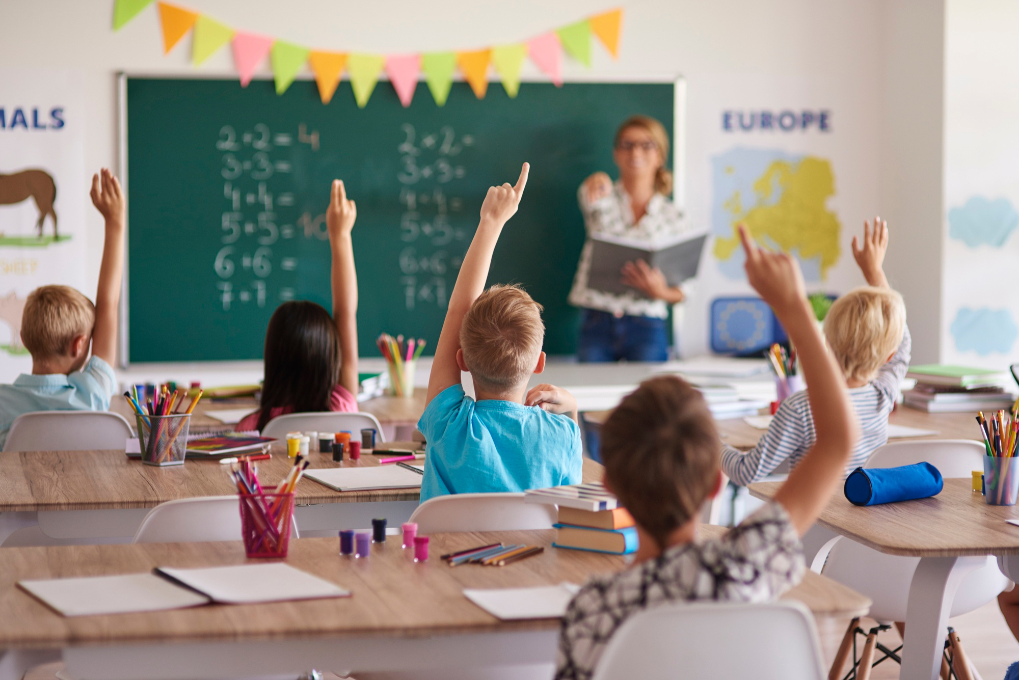 teacher pointing to pupils with their hands raised to answer a question.